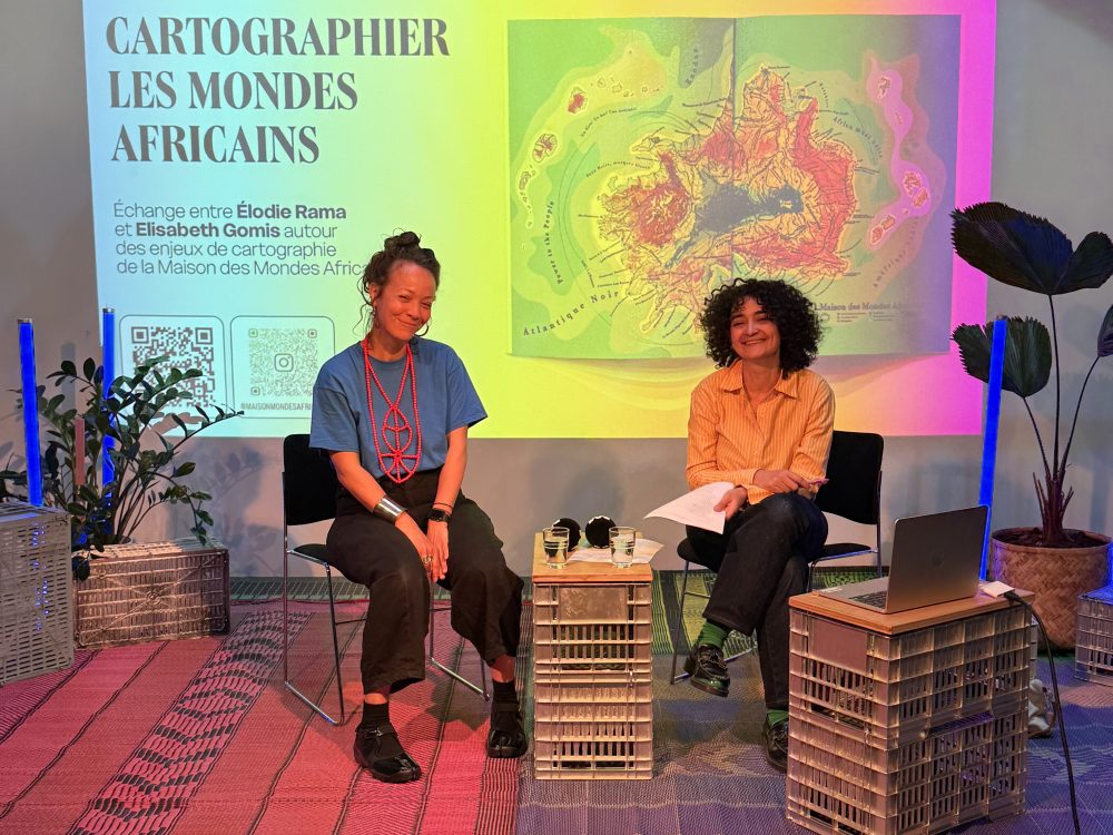 Elodie Rama et Zoubida Debbagh assises discutant posant devant un visuel visioprojeté de la carte Maison des Mondes Africains
